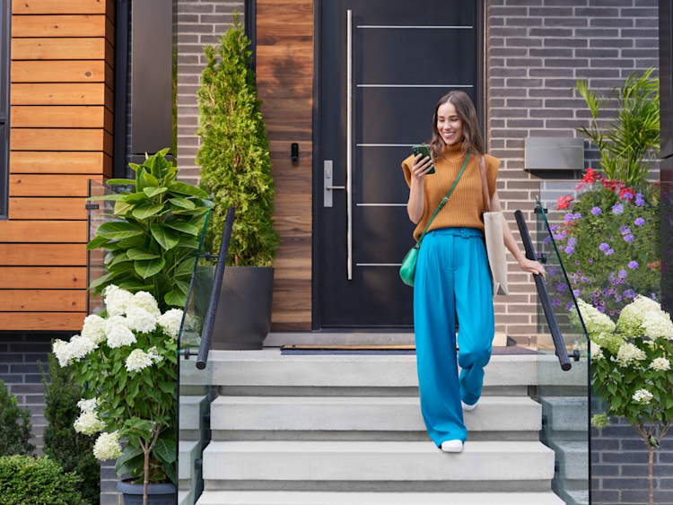 Woman exiting front of home checking her mobile phone with ecobee's Smart Doorbell Cameras visible.