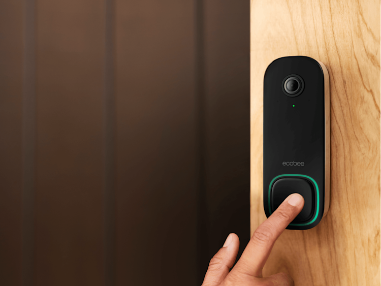 Close-up of a hand pressing ecobee Smart Doorbell Camera at a modern home with a brown front door.