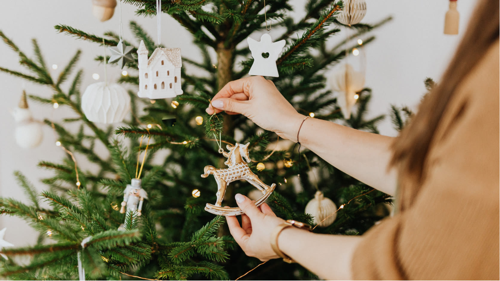 Woman adding a rocking horse ornament to her decorated Christmas tree