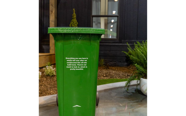 Picture of green bin in front of net-zero home with text "Everything you see here is what's left over after we constructed this off-site built home. There's not much to look at, which is pretty beautiful."