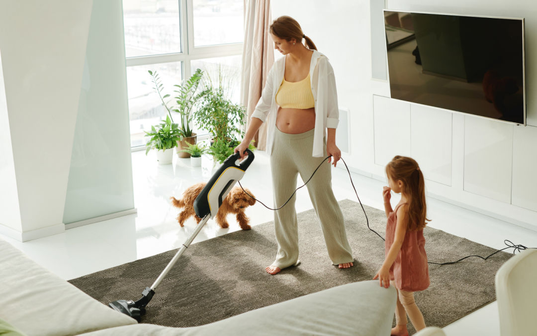 Woman vacuuming her living room, with dog and child beside her.