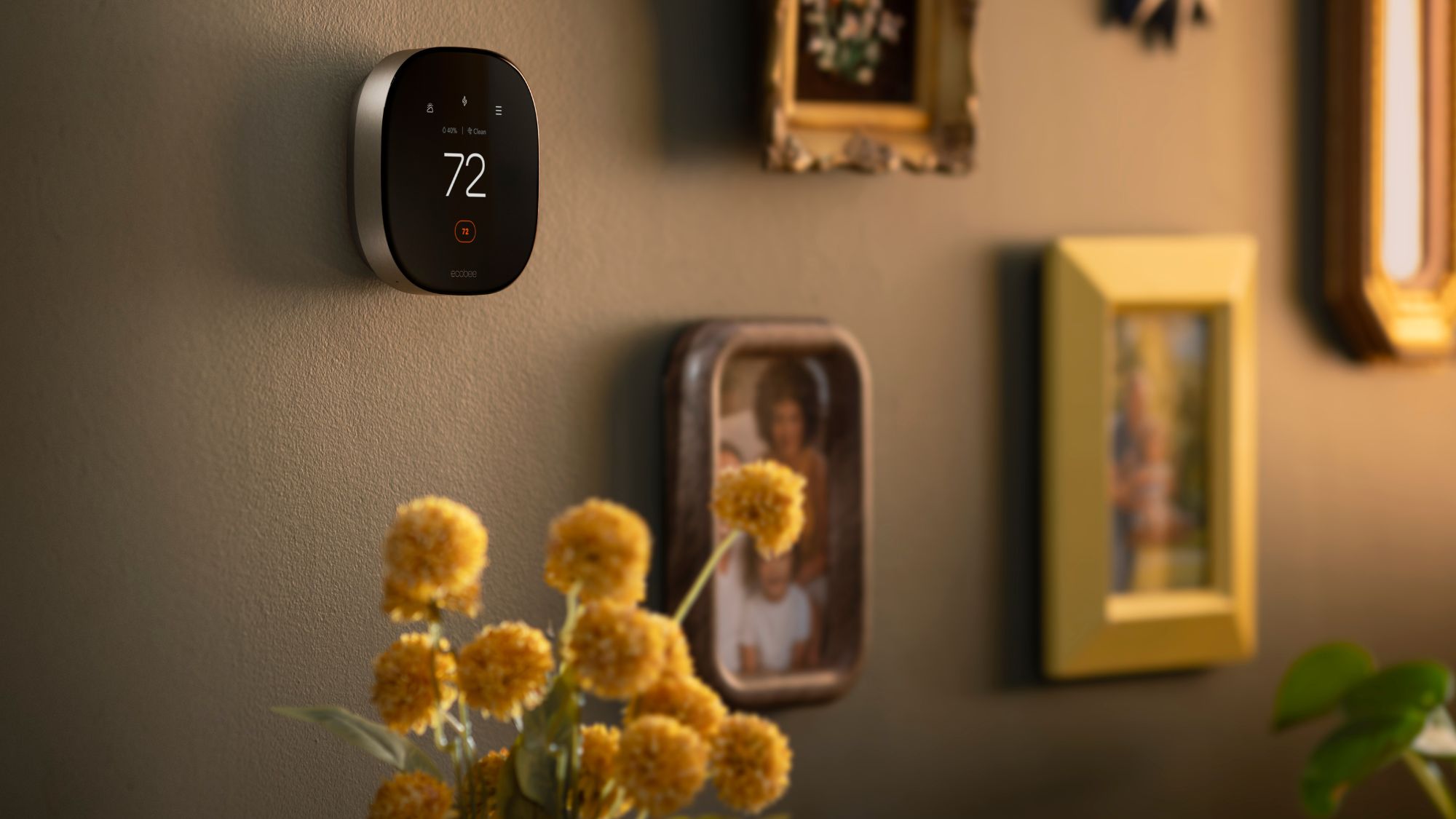ecobee Smart Thermostat Premium displaying 72°F on a wall surrounded by framed photos and artwork.