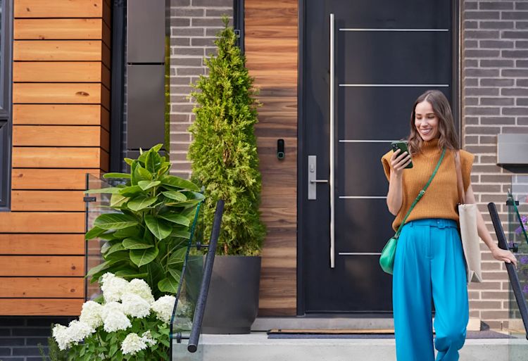Une femme sort de son domicile et vérifie son téléphone. Une notification de l'application ecobee indique : « Voulez-vous armer votre domicile ? »