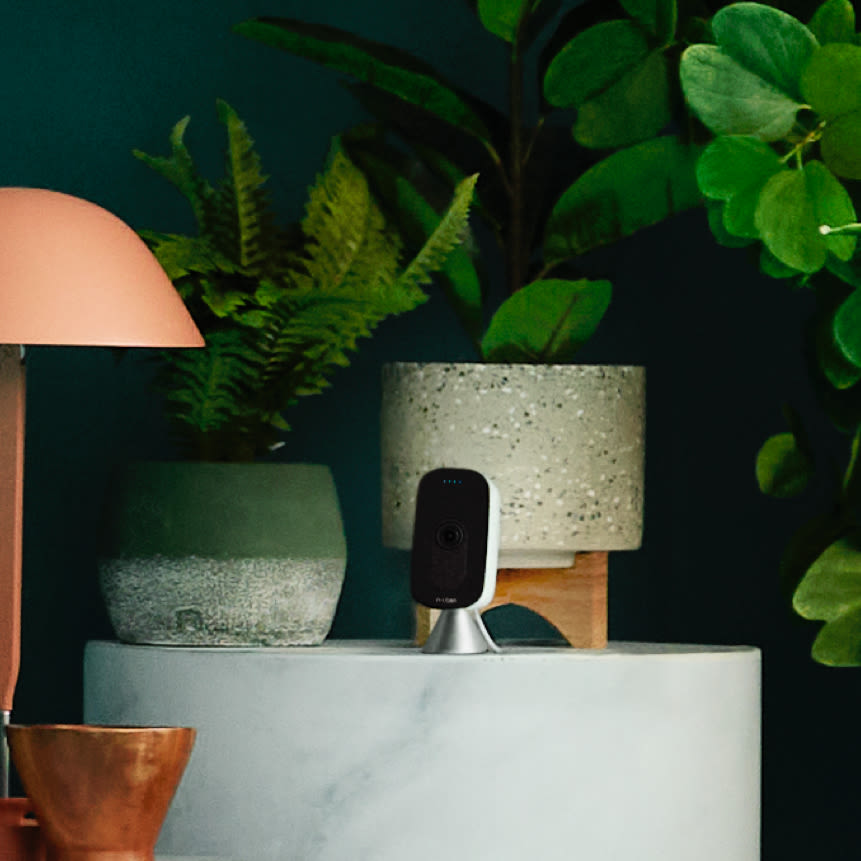 SmartCamera with voice control set on marble side table among potted greenery.