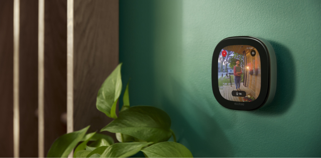 A Smart Thermostat Premium mounted on the wall, with the screen showing a woman standing at the front door, captured by ecobee's Smart Doorbell Camera.