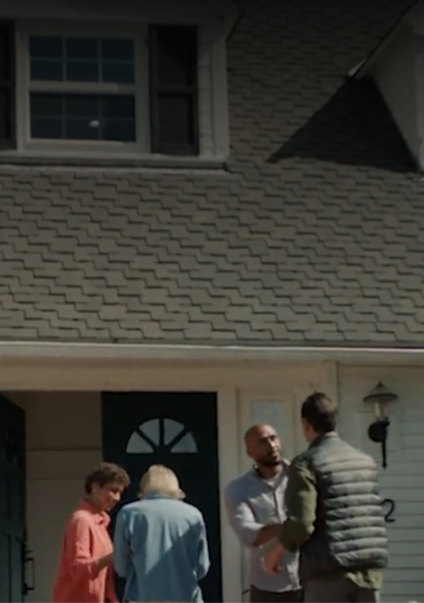 A husband and wife welcome a new couple to the neighborhood. The husbands shake hands near the “sold” sign on the lawn while the wives head in through the open door.