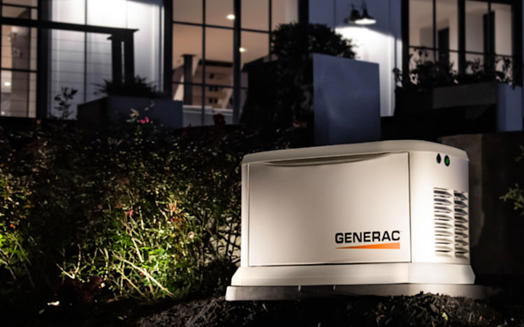 A Generac Generator in front of a home with a soft spotlight on it during the evening.