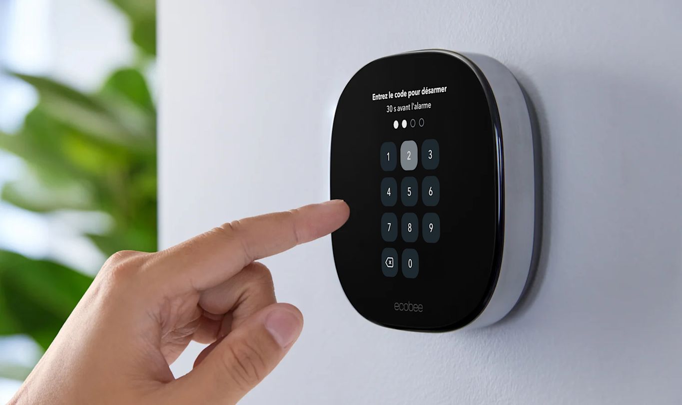 Une main saisit un code NIP sur un thermostat intelligent Premium d'ecobee fixé au mur.