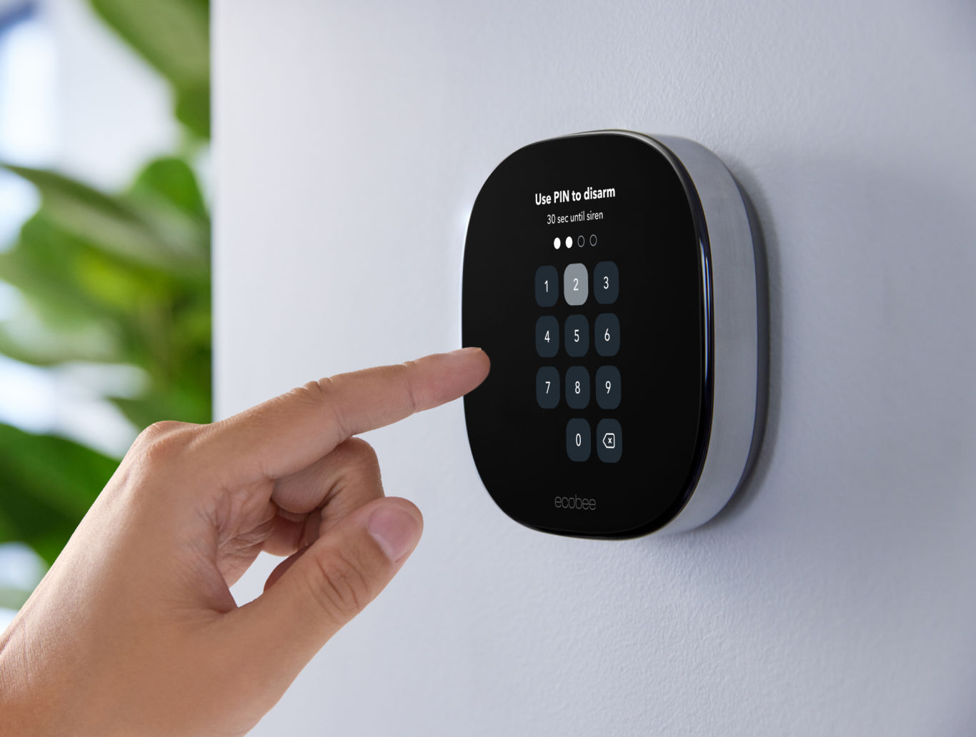 A hand reaches out to enter a pin code on an ecobee SmartThermostat Premium mounted on a wall