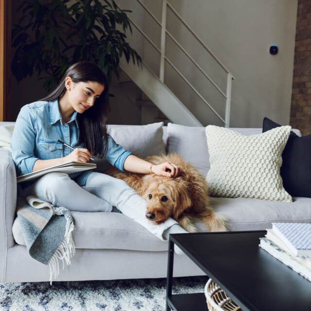 A woman sits on a couch with a dog; an ecobee thermostat is on the wall in the background.