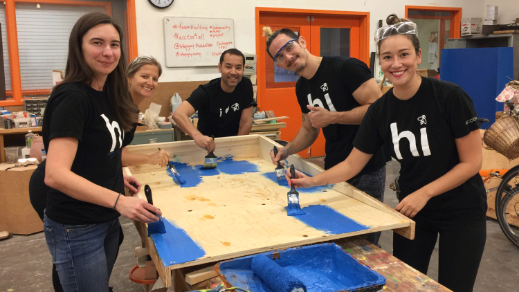 Five ecobee employees wearing ecobee "Hi" t-shirts painting a wooden accessibility ramp the colour blue