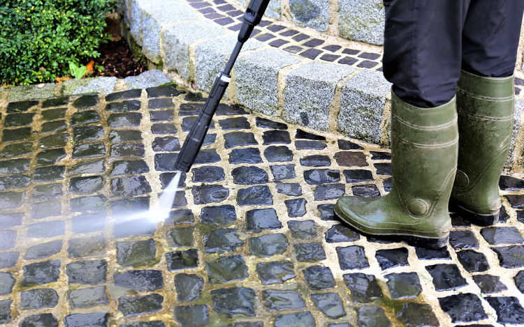 A person uses a pressure washer on an outdoor stone floor.