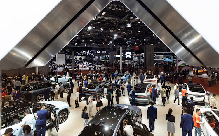 A showroom at an electric vehicle car show displaying several electric cars with modern designs, bright lighting, and attendees exploring the vehicles.