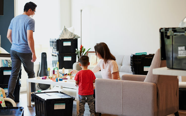 Young boy and mom play with train set in cluttered family room. 