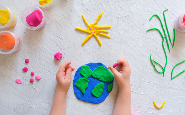 A child making an Earth out of clay. There is also a yellow sun made out of clay above the Earth. 