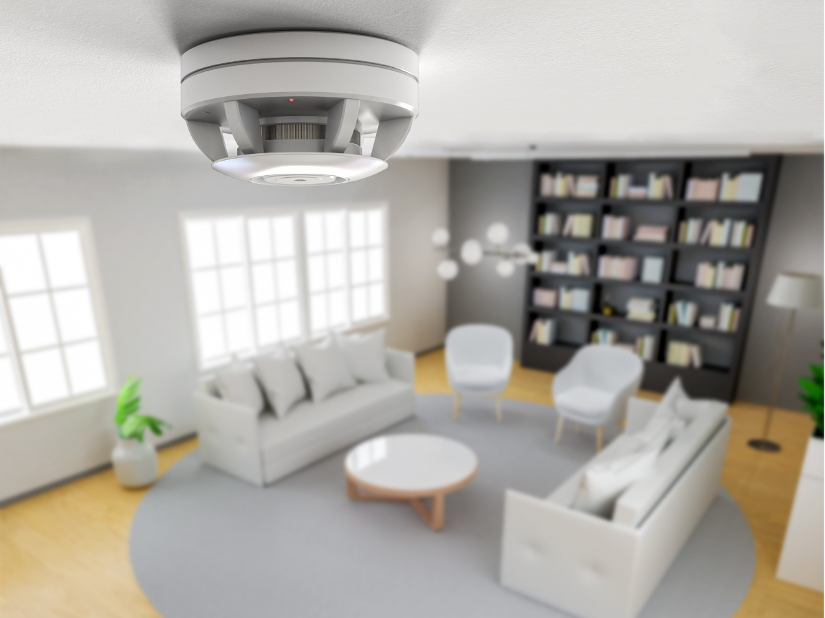 A white smoke detector installed on the ceiling in a living room in a modern home. 