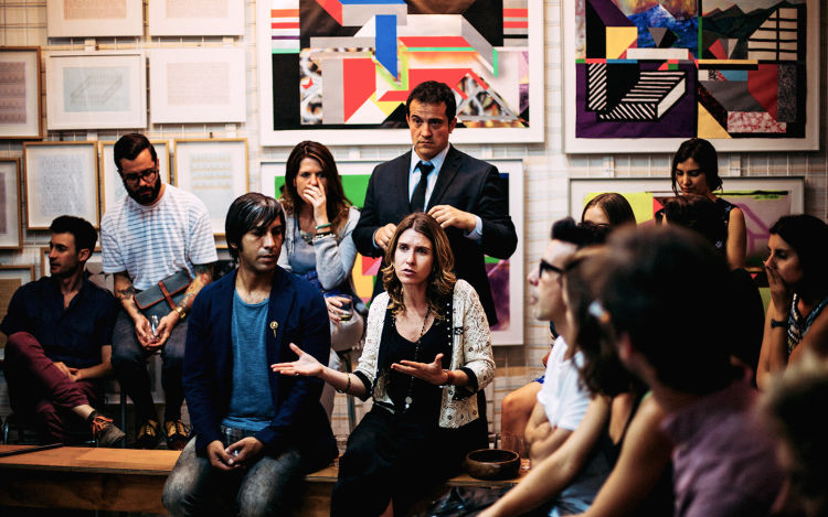 Group of people having a serious conversation in a room with framed art behind them. 