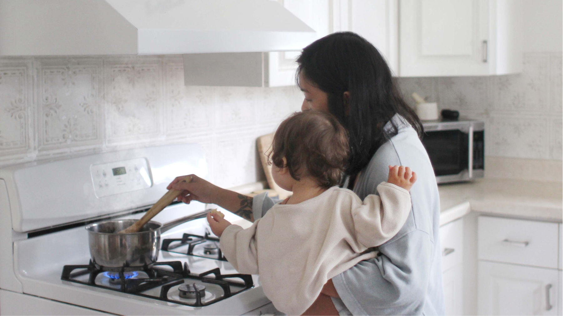 Woman carrying her child and cooking over a gas stove.