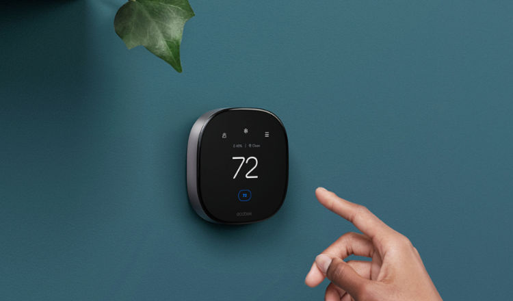 A hand reaches for an ecobee thermostat on a wall