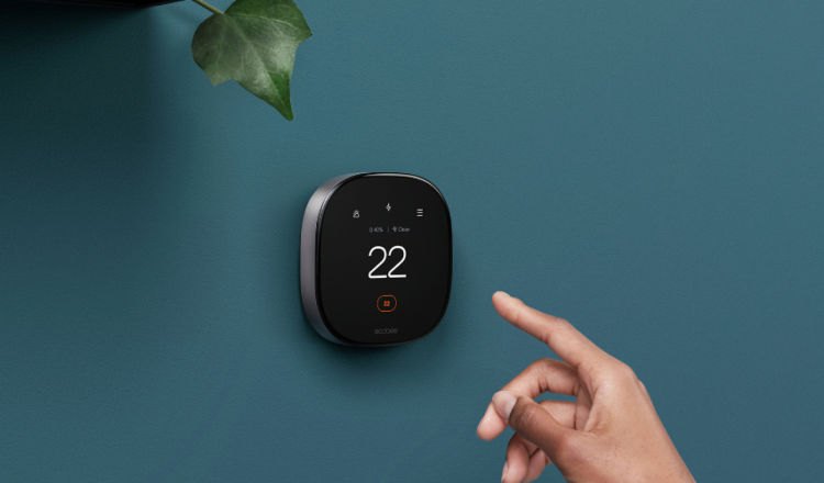 A hand reaches for an ecobee thermostat on a wall