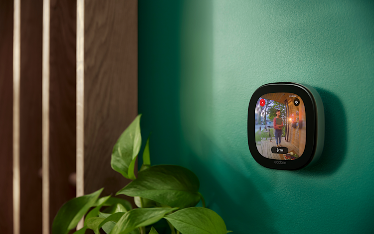 ecobee's Smart Thermostat Premium showing the live view of ecobee's Smart Doorbell Camera. The thermostat is installed on a green wall in a modern home.