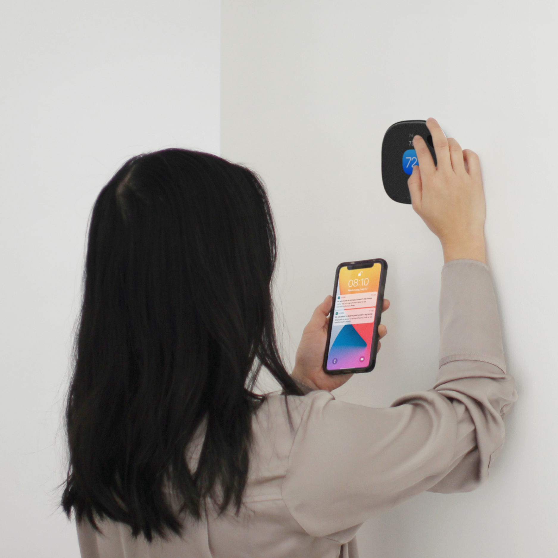 a person adjusts their thermostat while looking at their phone