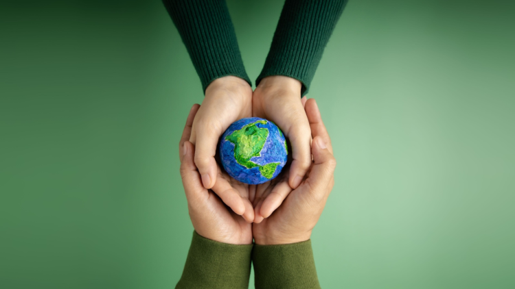 Kids and adult set of hands holding a tiny Earth against a green background. 