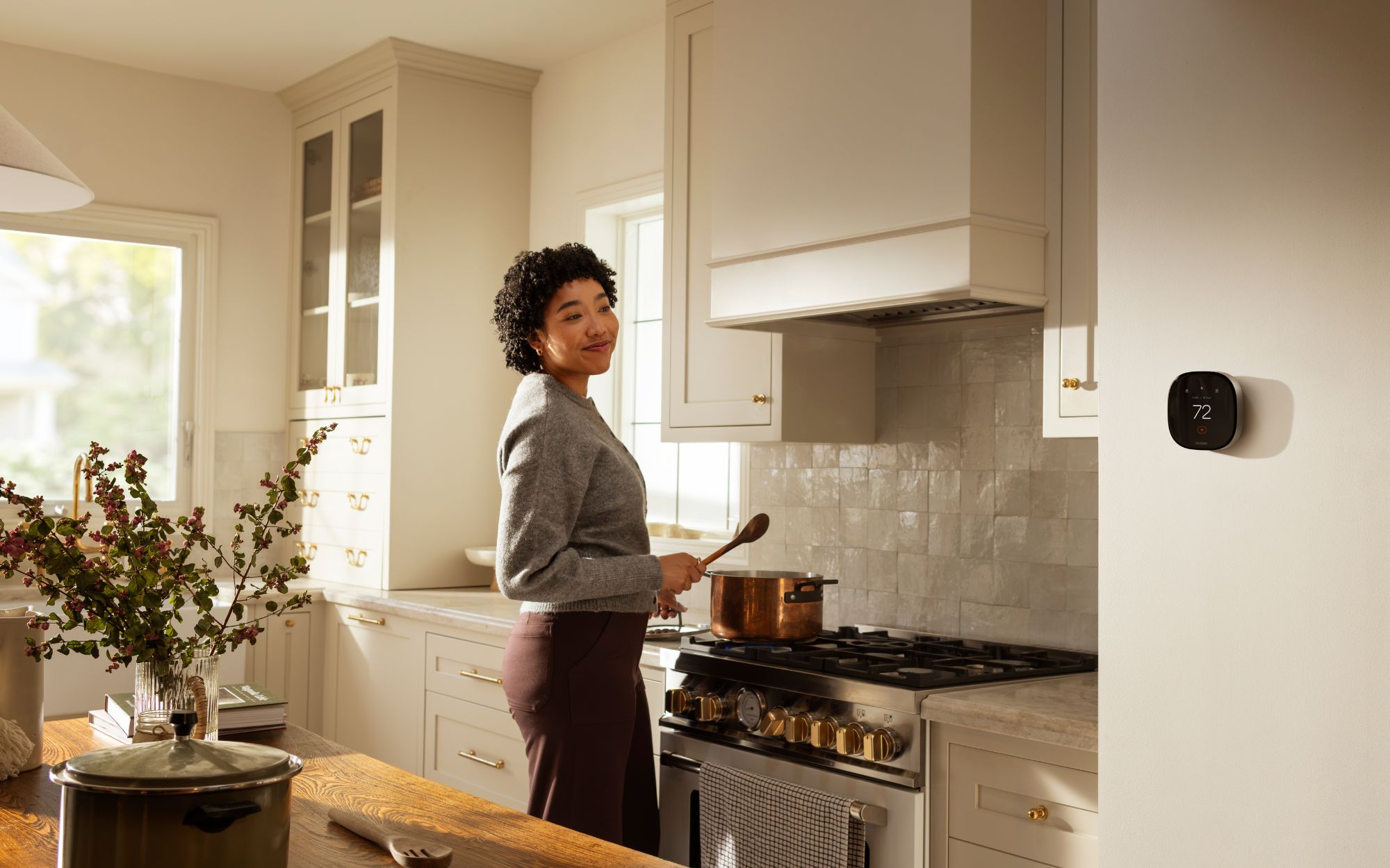 Woman cooking at a stove in a bright kitchen with an ecobee Smart Thermostat displaying 72°F on the wall.
