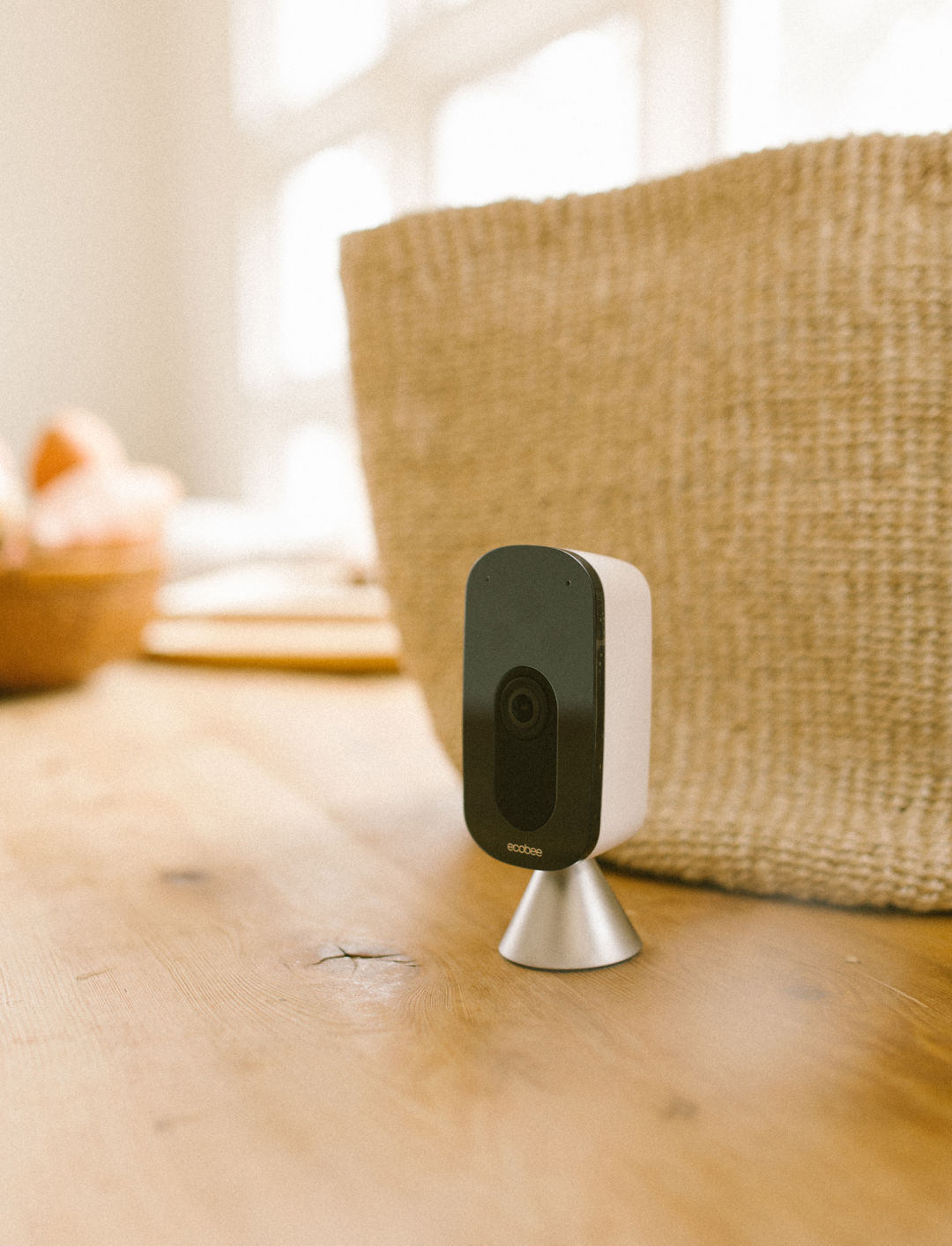 Image of a ecobee SmartCamera on a countertop in-front of a basket. 