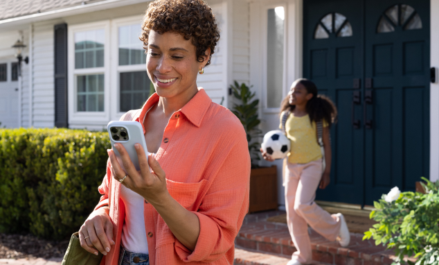 woman looks at her phone as a child leaves the house behind her