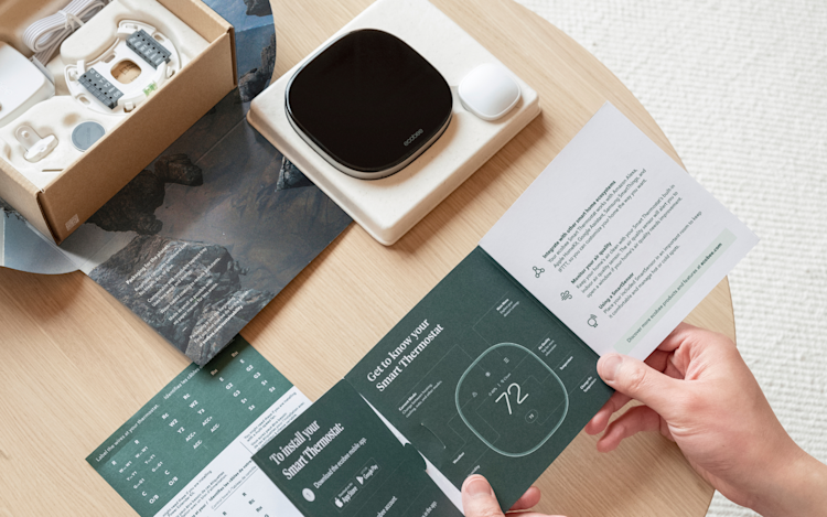 A person opening ecobee's Smart Thermostat Premium, with the packaging and thermostat with SmartSensor on display