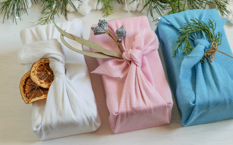 Three presents wrapped on a table using sustainable materials, including cloths and dried orange slices.