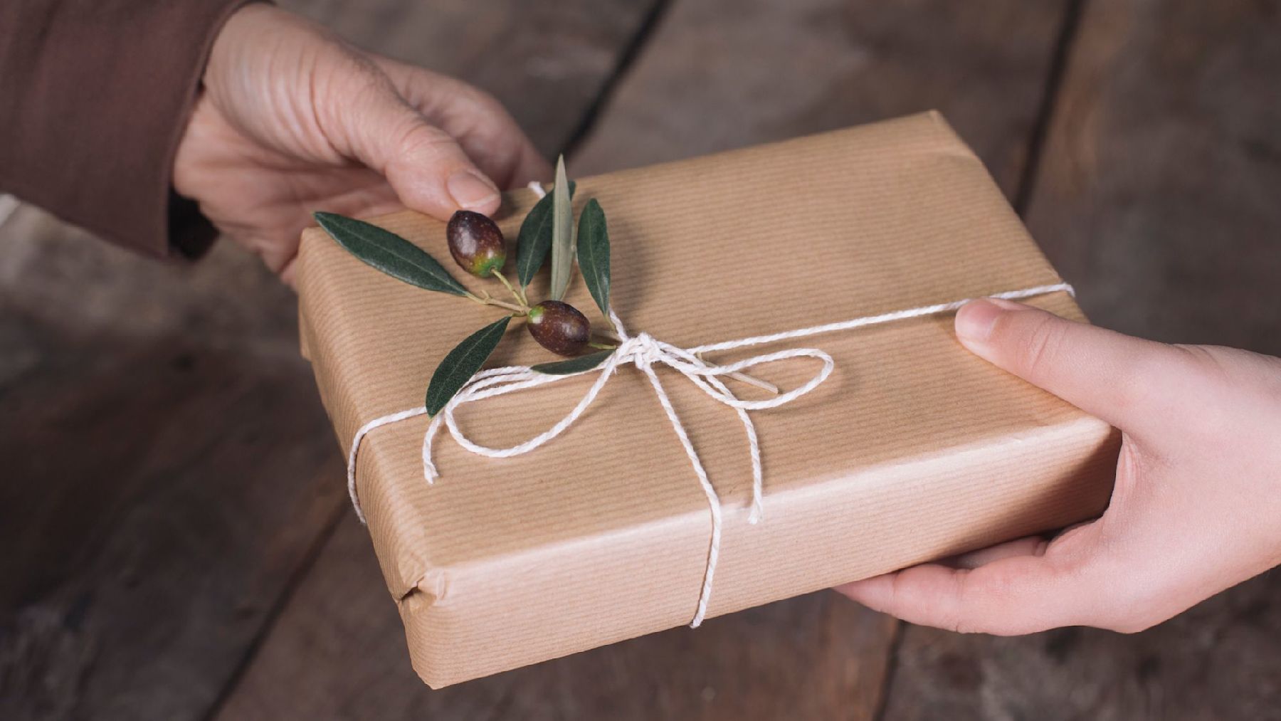 A gift wrapped in sustainable wrapping with brown paper, string, and a sprig of holly.