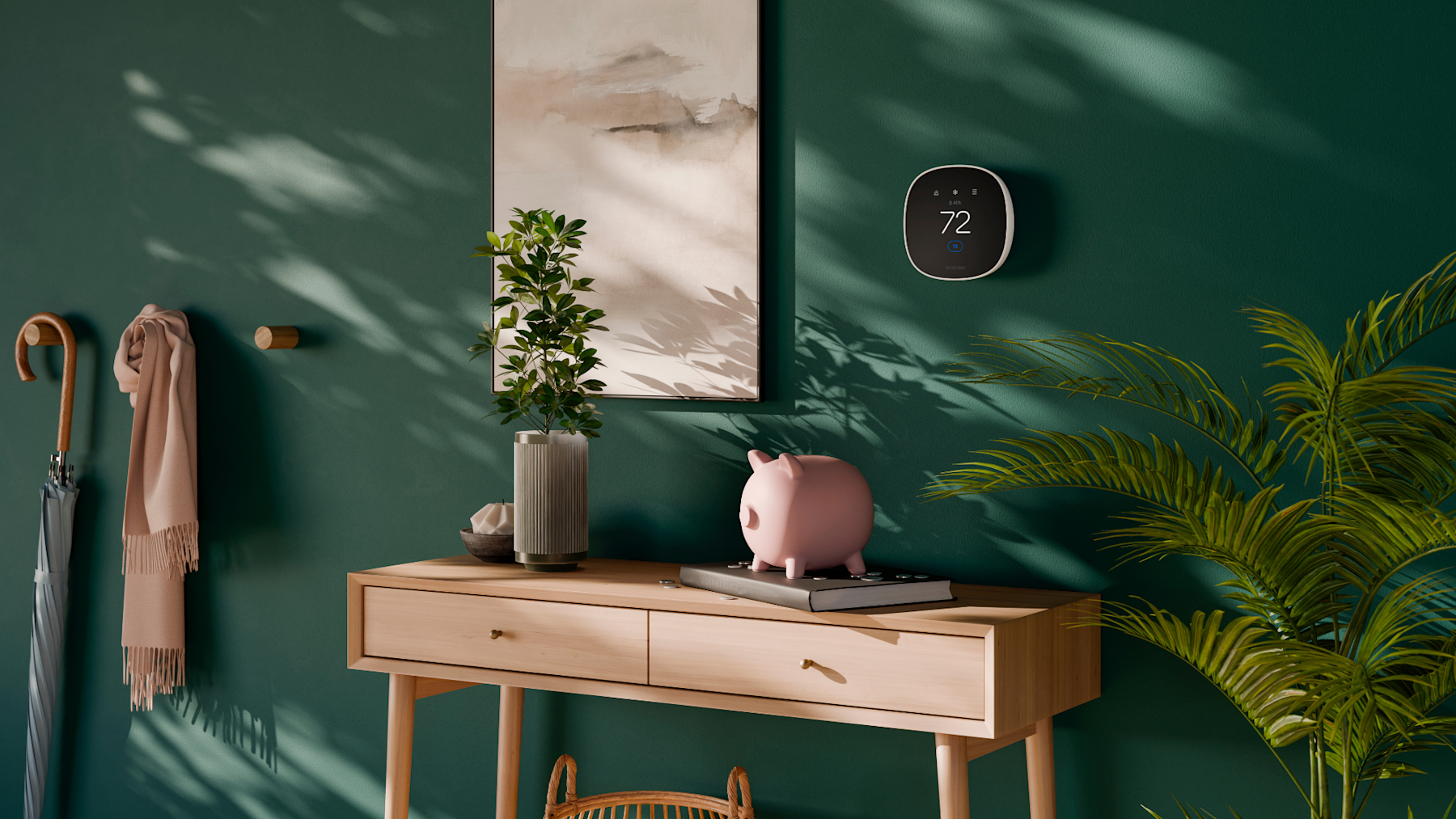 ecobee's Smart Thermostat Essential is installed in a home with a dark green wall, a plant, a small side table and a painting beside the thermostat.