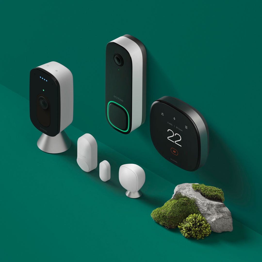ecobee thermostat, Smart Doorbell Camera, SmartCamera with voice control and sensors sitting on a green background near a grassy rock.