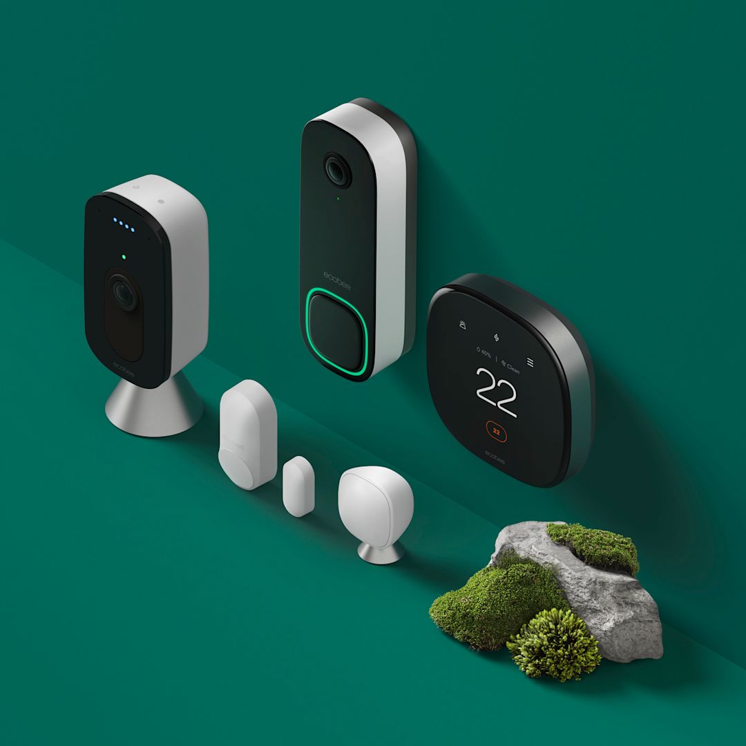 ecobee thermostat, Smart Doorbell Camera, SmartCamera with voice control and sensors sitting on a green background near a grassy rock.