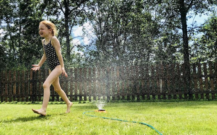 A young girl playing in a water sprinkler to cool herself down from the heat