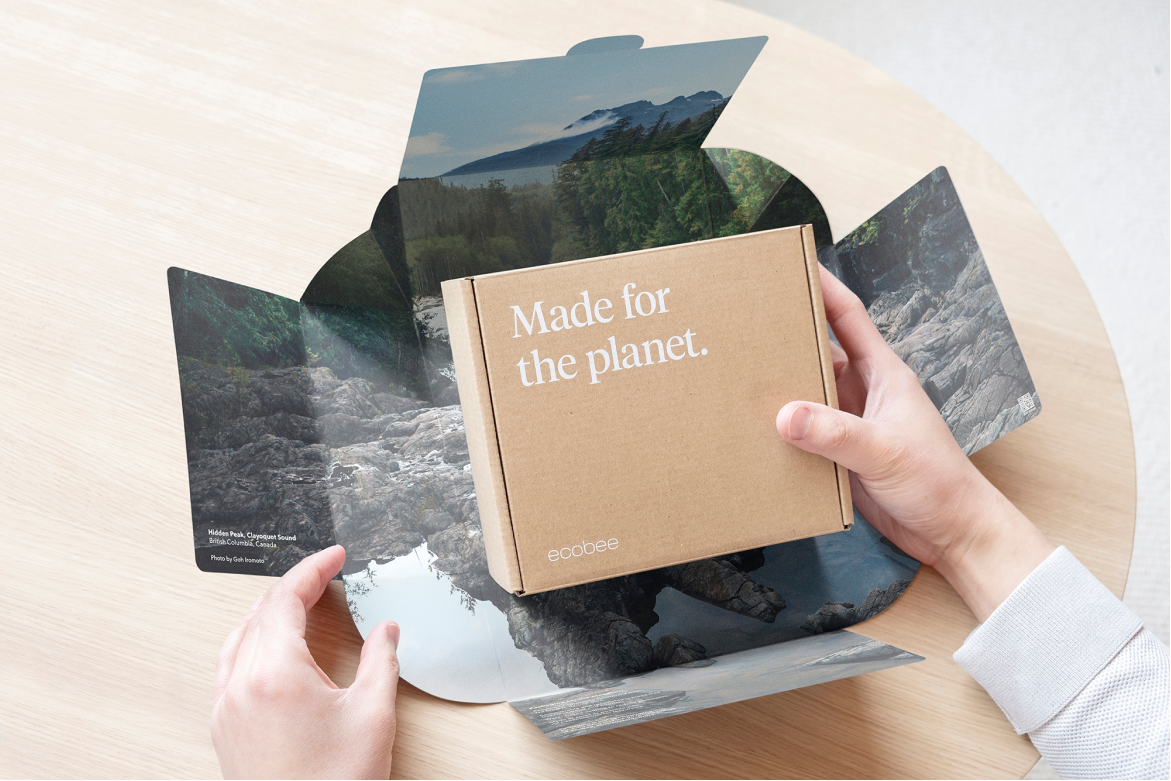 A pair of hands opens the box for ecobee Smart Thermostat Premium, showing the interior of the box has an image of trees and a river.