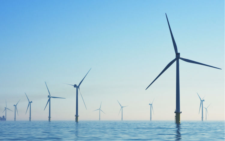 Image of an offshore wind farm, with several wind turbines in a body of water.