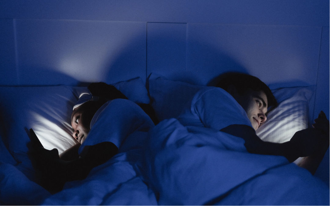 Couple looking at cell phones in bed, in the dark.