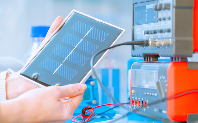 A scientist testing a battery in a laboratory, with the battery placed on a testing device and various scientific equipment visible in the background.