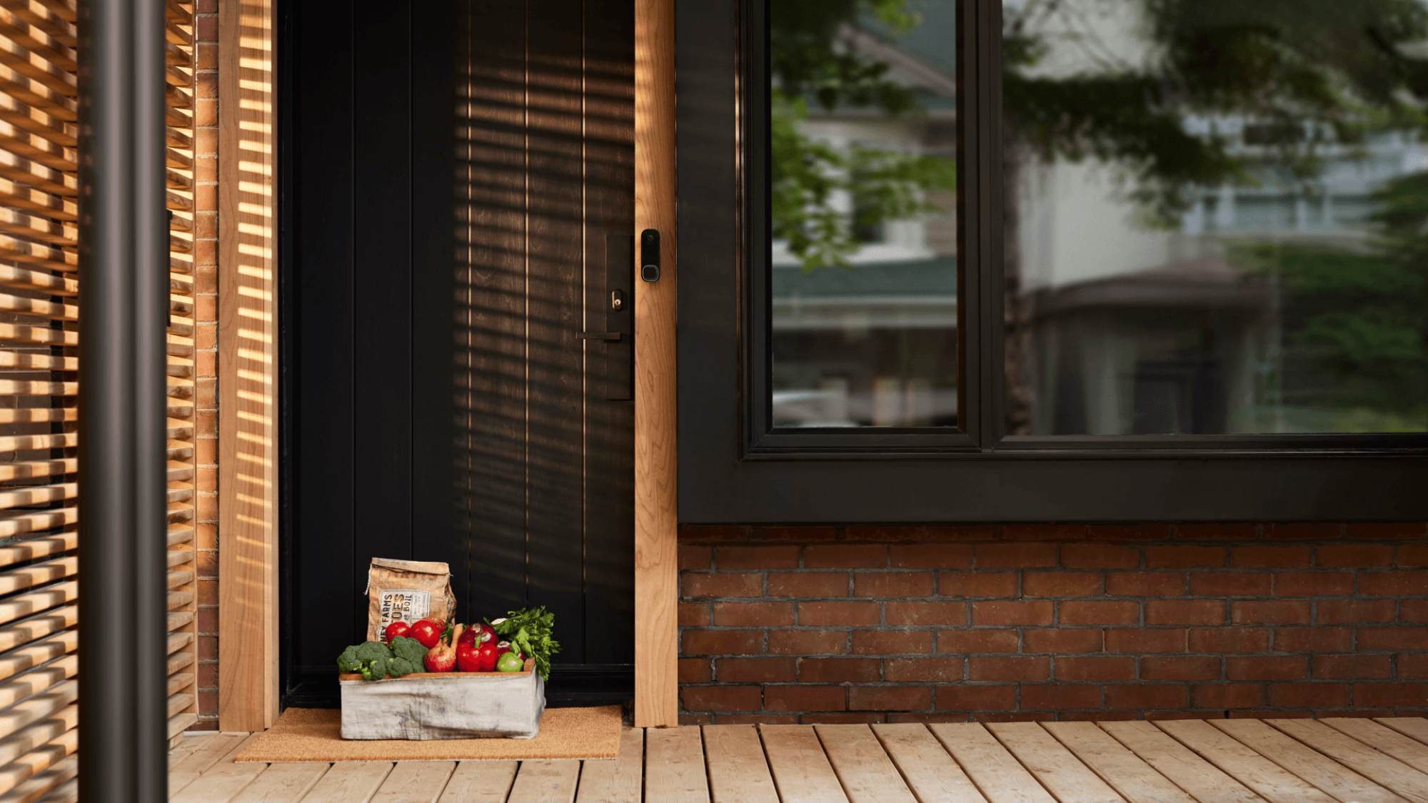 The front porch of a modern home with a dark brown door, an ecobee Smart Doorbell visible and a fresh produce delivery sitting outside the door. 