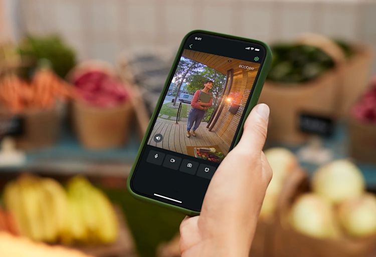 Une main tient un téléphone, qui montre quelqu’un à la porte d’entrée.