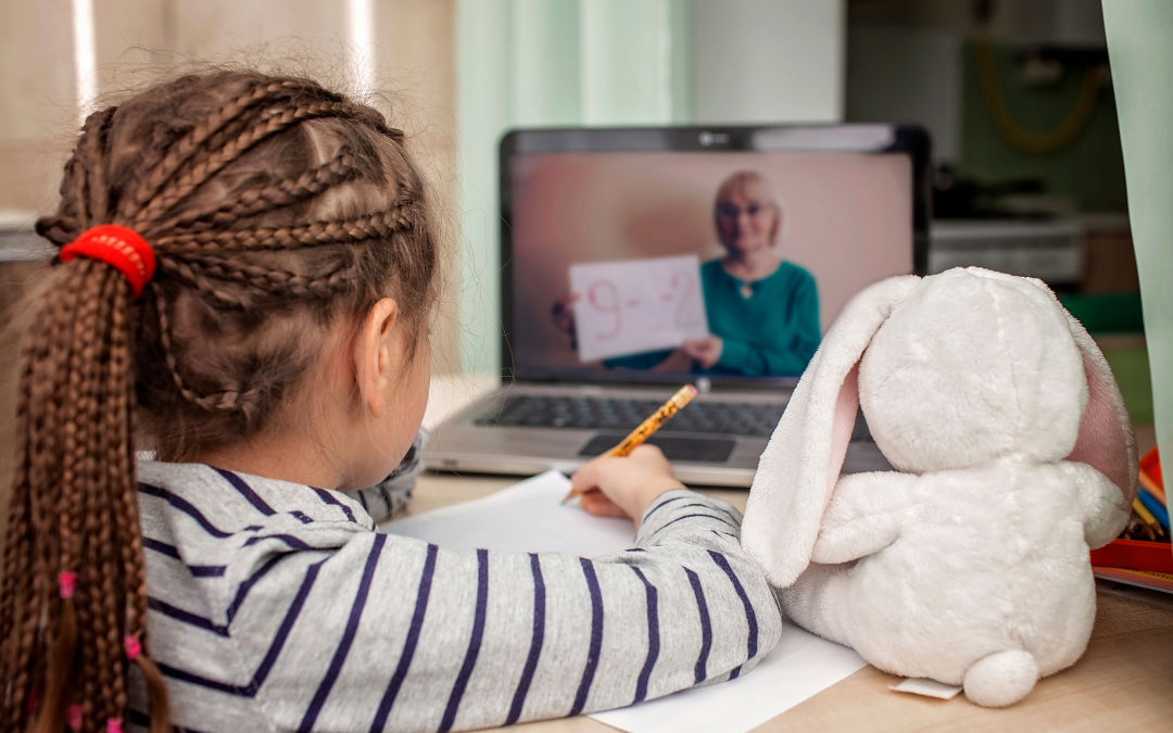 A child watches a teacher on a laptop screen.