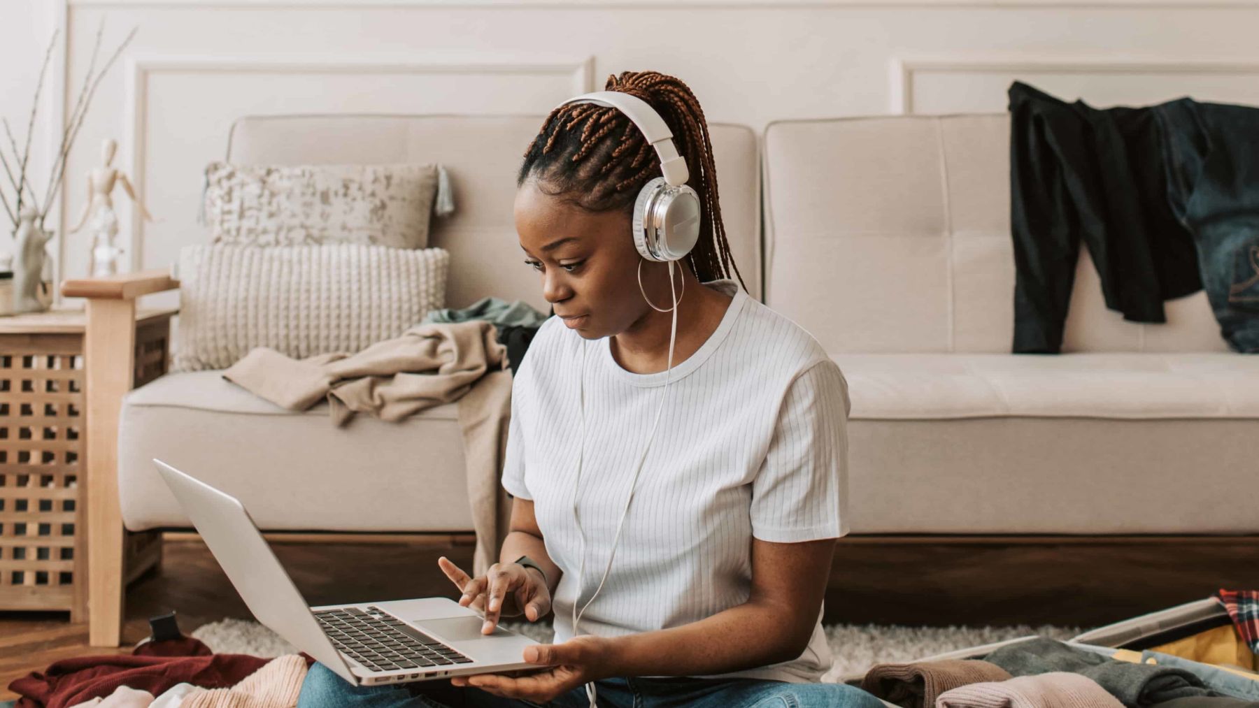 Woman listening to her headphones while working on her laptop in front of her couch.