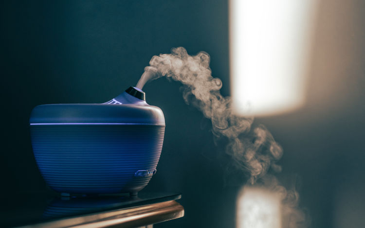 A blue humidifier on table releasing water vapor. 