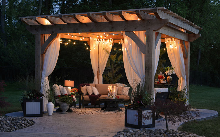 A backyard gazebo with lights and comfy seating at dusk.