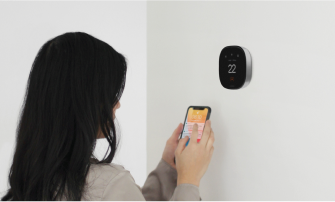 A person checks their phone while in front of an ecobee thermostat