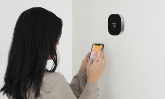 A person checks their phone while in front of an ecobee thermostat