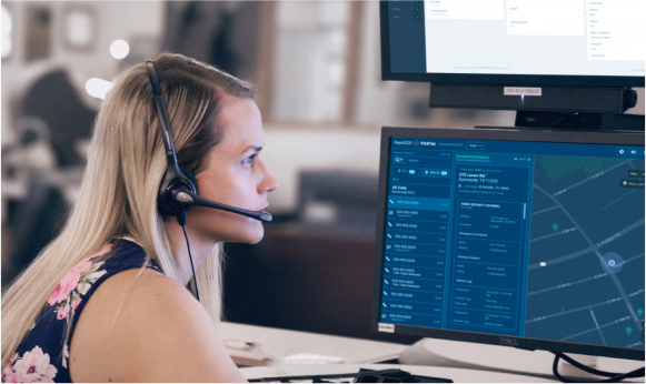 Woman wearing a headset sitting in front of a computer screen monitoring activity.